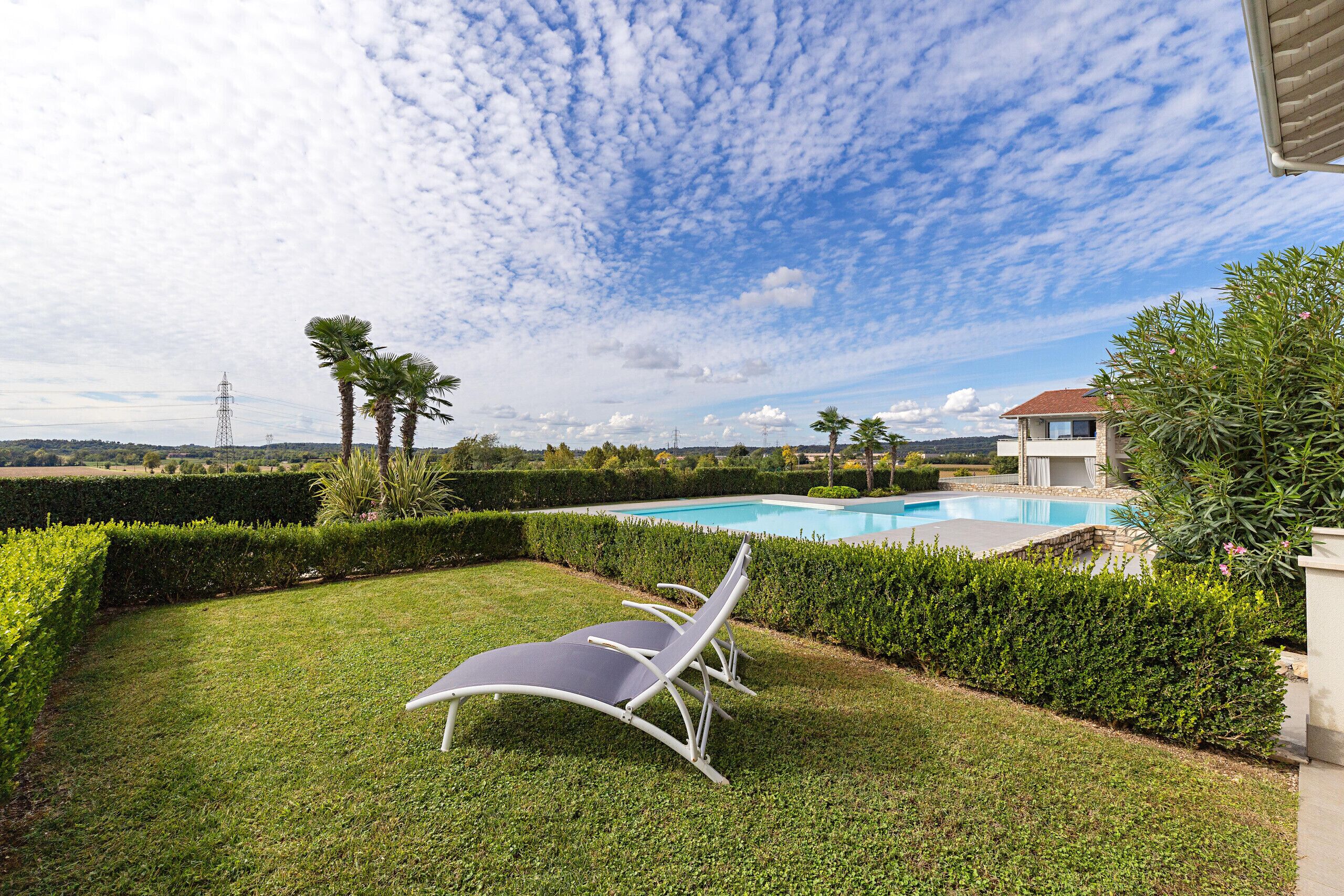 A poolside area with a clear view of the pool, a well-maintained lawn, and a modern outdoor chair.