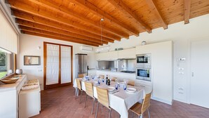 Un comedor amplio con techo de madera, una cocina con electrodomésticos modernos y un ventanal grande que proporciona luz natural.