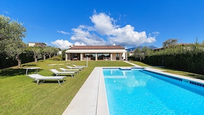Una piscina con sillas de descanso, una casa al fondo y un cielo azul despejado.