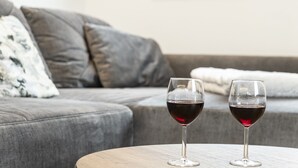 Two wine glasses on a round wooden table in a living room with a grey sofa and a white pillow. - Alpine Apartment With View & Garden (Wildschönau)