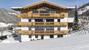 A multi-story hotel with wooden balconies, a ski slope in the background, and a snowy landscape. - Alpine Apartment With View & Garden (Wildschönau)