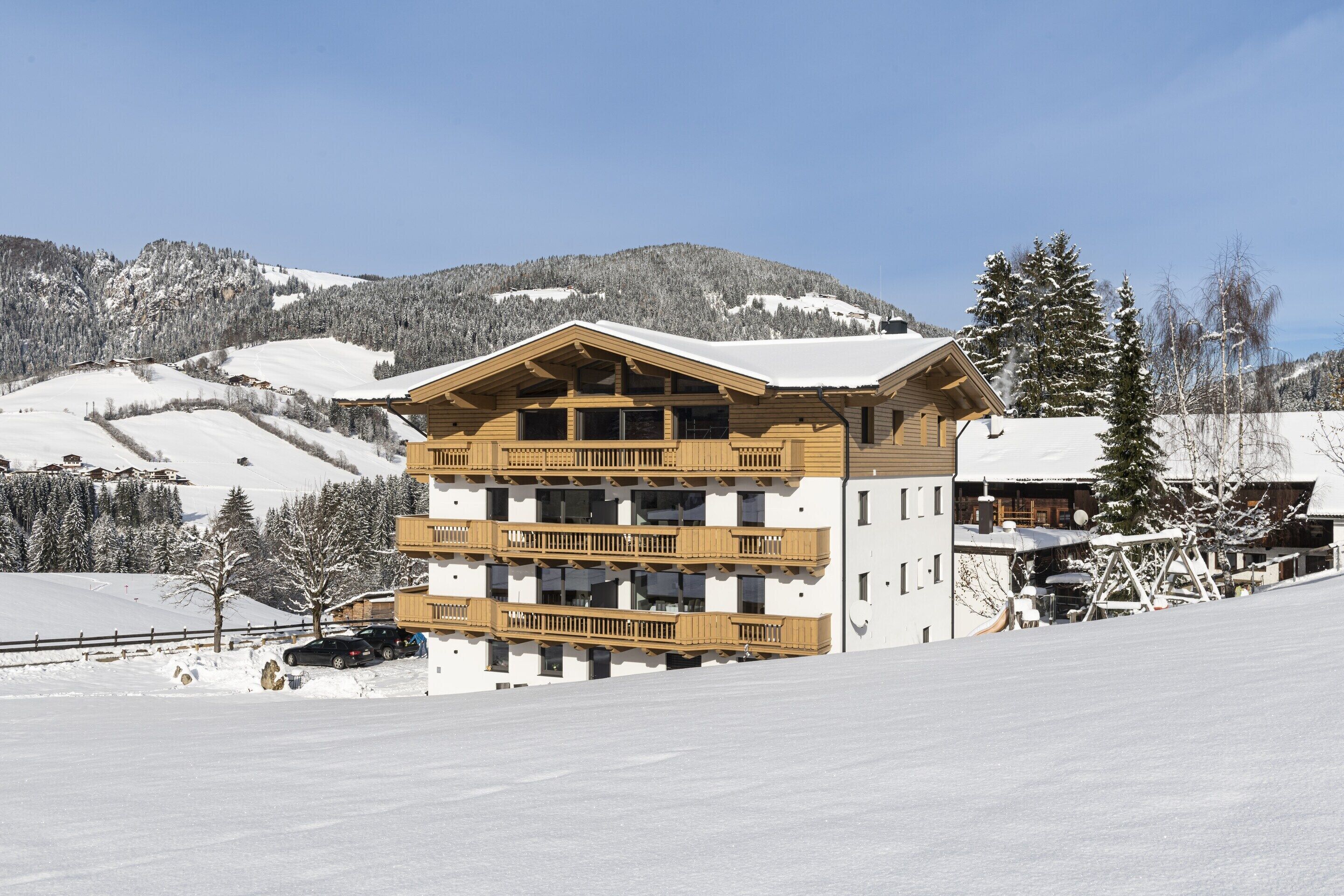 Un edificio de madera de varios pisos con balcones, con una imponente montaña nevada de fondo.