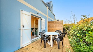 Une terrasse avec une table ronde et quatre chaises, une clôture en bois et un bâtiment bleu avec une porte blanche.