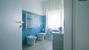 Et moderne badeværelse med en blå accentvæg, et hvidt badekar, en bidet, et toilet og en vask.