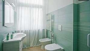 Et badeværelse med en hvid vask, en bruser samt et toilet.