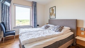 Una camera da letto con un letto, una sedia, un comodino, una finestra e un quadro appeso al muro.