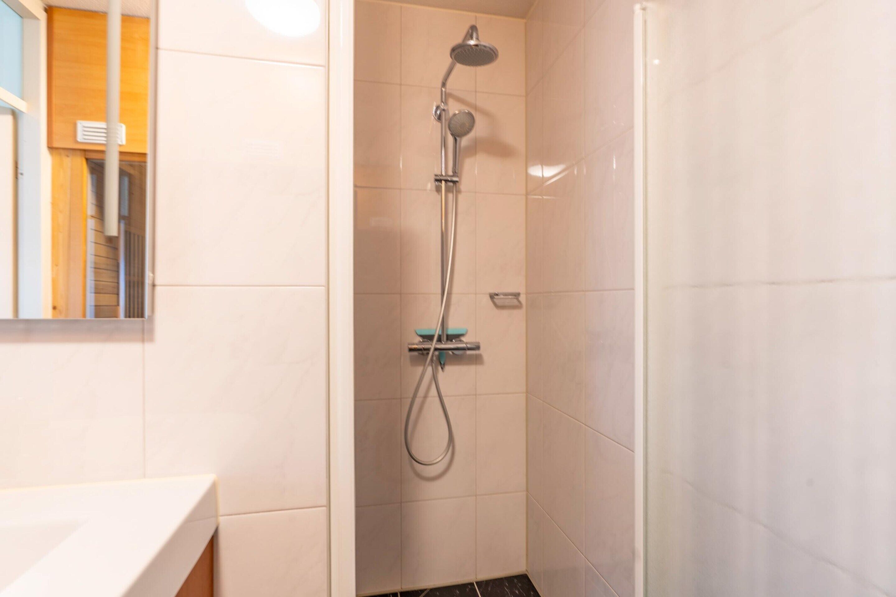 Piccola cabina doccia con soffione a mano e lavabo mobile.