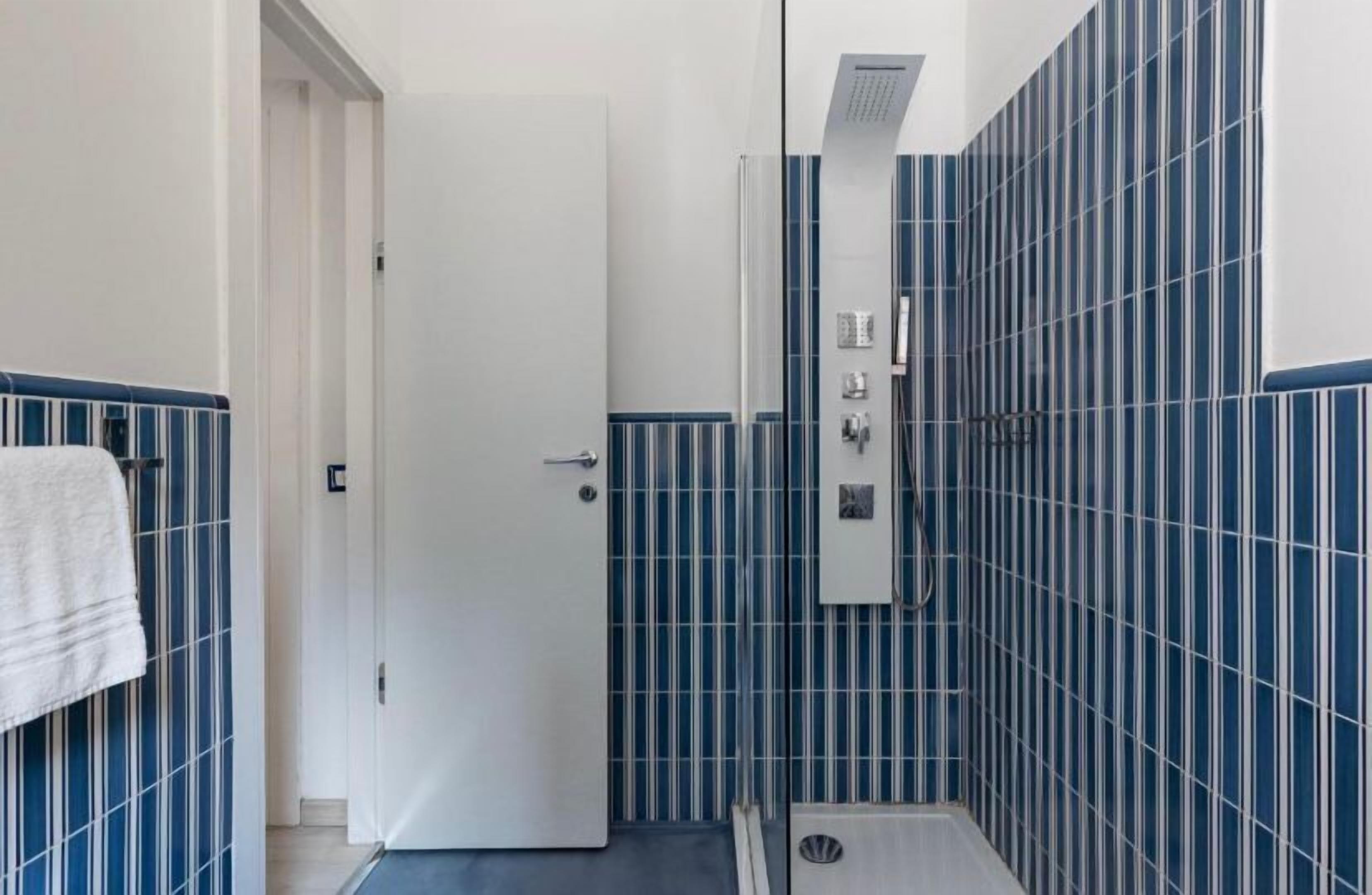 A bathroom with a white door, blue-striped tiles, a shower area, and a towel rack.