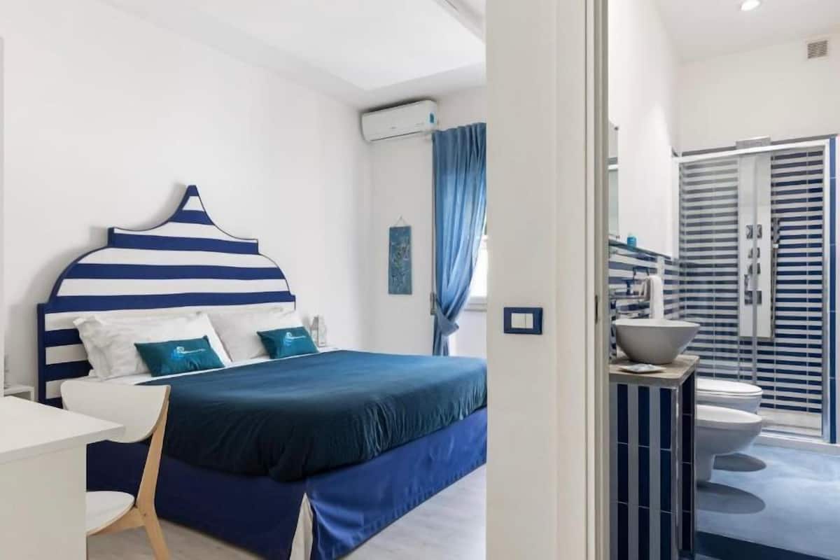 Un dormitorio moderno con un cabecero a rayas, una mesita de noche y vistas al baño.