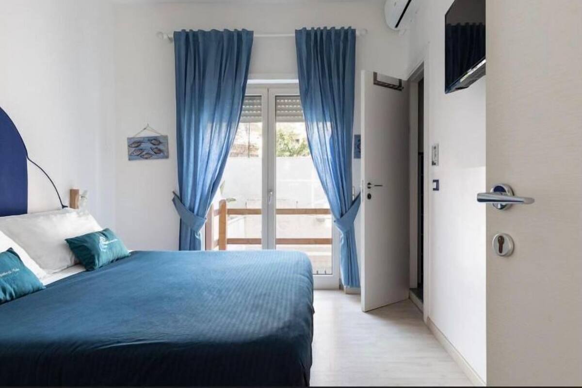 Un dormitorio con cama, cortinas, una puerta y vistas a través de un ventanal.