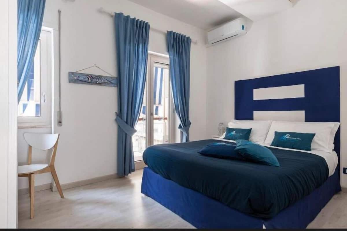 Un dormitorio con una cama grande, cortinas azules, una silla blanca y aire acondicionado instalado en la pared.