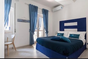 Una camera da letto con un letto grande, tende blu, una sedia bianca e un condizionatore d'aria a parete.