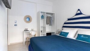A bedroom with a bed, a white wardrobe, a small desk, and a wall-mounted mirror.