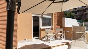 An outdoor patio area with a table and chairs, a large umbrella, and a view of a building in the background.