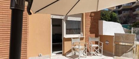 An outdoor patio area with a table and chairs, a large umbrella, and a view of a building in the background.