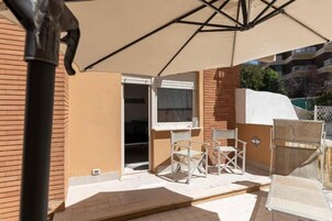 Un'area patio all'aperto con tavolo e sedie, un ombrellone e vista su un edificio sullo sfondo.