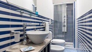 A bathroom with blue and white striped tiles, a large white sink, a toilet, and a glass shower enclosure.