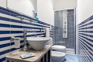 Un bagno con piastrelle azzurre e bianche a righe, un lavandino bianco grande, un water e un box doccia in vetro.