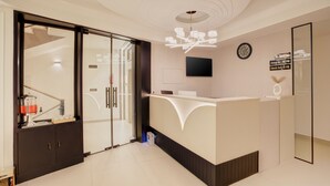 A modern reception area with a glass door entrance, a reception desk, a wall-mounted TV, and a clock. - Hotel Urban chant (Rishikesh)
