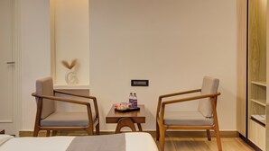 A hotel room with two wooden chairs, a small table with snacks and drinks, a wall-mounted light, and a door. - Hotel Urban chant (Rishikesh)