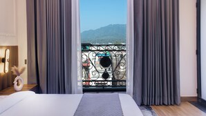 A bedroom with a large bed, grey curtains, and a balcony with a metal railing. - Hotel Urban chant (Rishikesh)