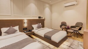 A hotel room with two beds, a small seating area with chairs, a nightstand, and an air conditioning unit. - Hotel Urban chant (Rishikesh)