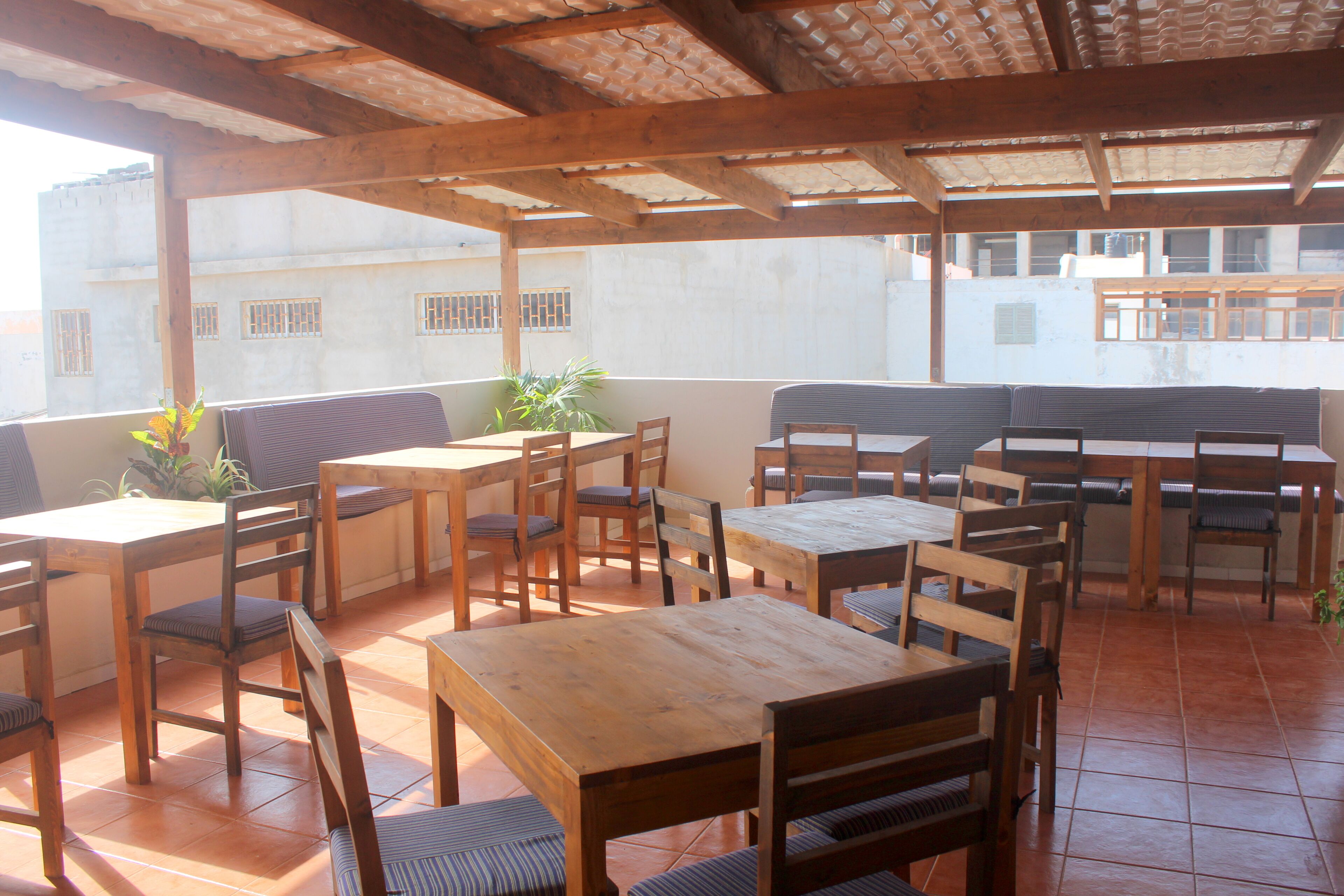 An outdoor patio with wooden tables and chairs, potted plants, and a view of buildings in the background.