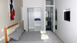 Una cama bien hecha con almohadas, una mesita de noche, un cuadro en la pared, un armario y un televisor también en la pared.