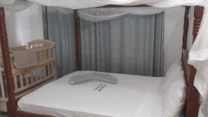 A single bed with a canopy, a wooden crib, and a curtain backdrop. - Pearl Apartments (Malindi)