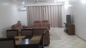 A living room with a sofa set, a dining table with chairs, a television on a wooden stand, and a curtain. - Pearl Apartments (Malindi)