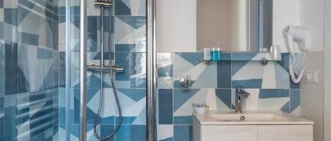 Un baño moderno con cabina de ducha de vidrio, tocador blanco y salpicadero de azulejos geométricos.