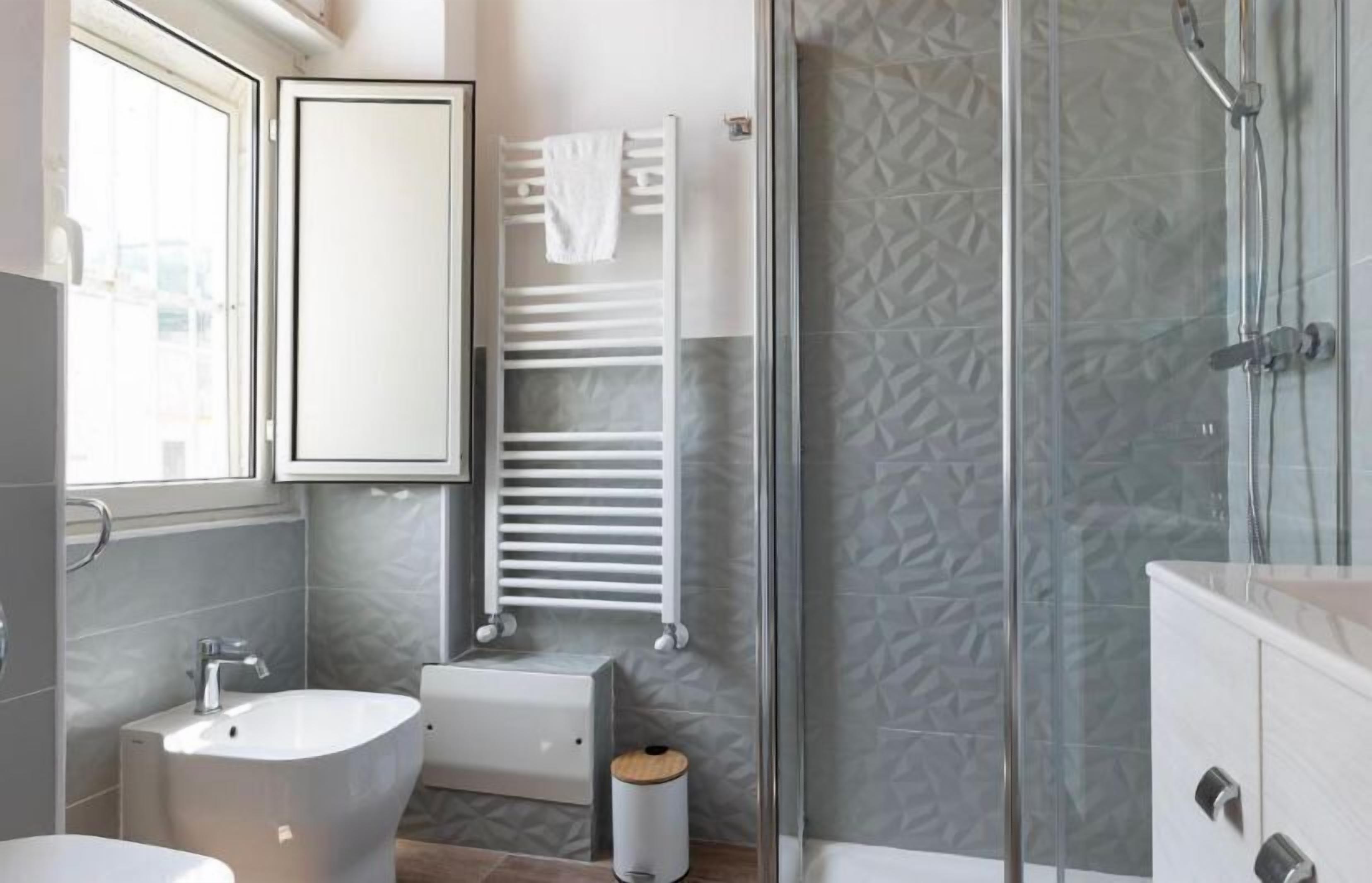 Un baño moderno con cabina de ducha de vidrio, un lavabo blanco y un perchero para toallas.