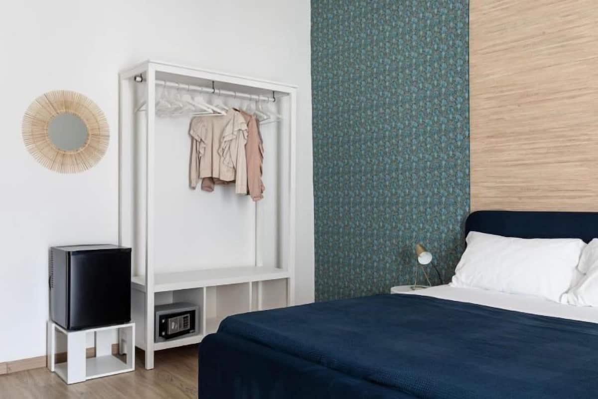 Un dormitorio con cama, un armario blanco, un televisor sobre un mueble bajo y una pared decorada.