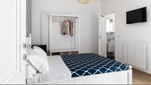 Un dormitorio con cama, armario, lámpara colgante y televisor en la pared.
