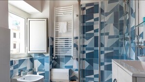 Un baño moderno con un rebozo de azulejos geométricos, una mampara de vidrio, un toallero blanco y un inodoro a la vista.