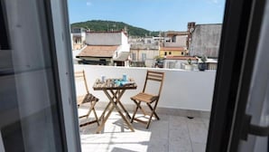 Un balcón con mesa y sillas, con vistas a un paisaje urbano que incluye edificios y una colina.