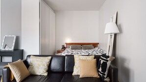 Ein modernes Hotelzimmer mit einem Bett, einem schwarzen Ledersofa, einem Nachttisch mit Lampe und einem Kleiderschrank.