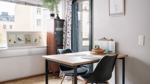 Ein Essbereich mit Tisch und Stühlen, ein Fenster mit Blick auf Gebäude, eine Pflanze und ein gerahmtes Bild an der Wand.