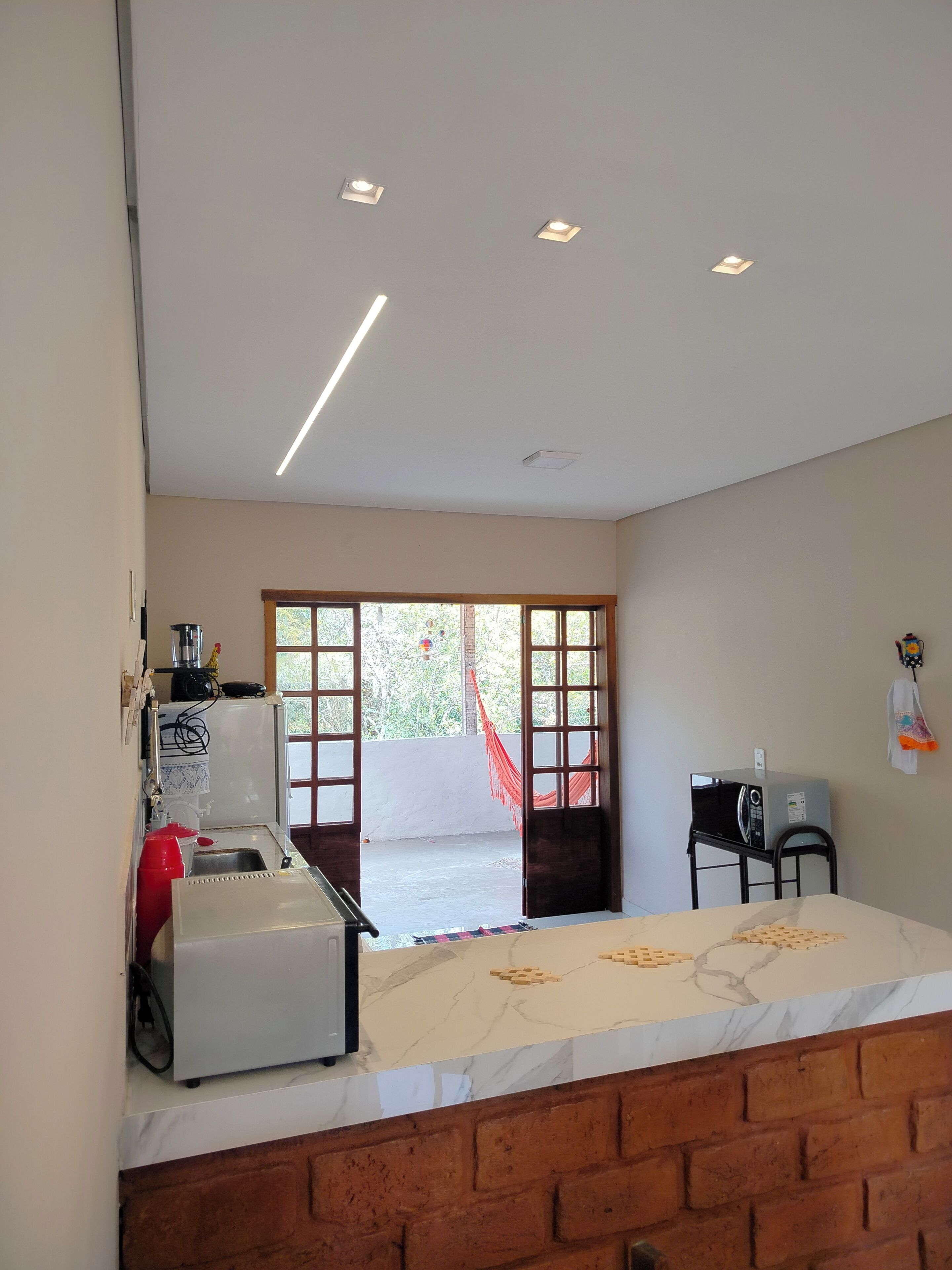 Una cocina con refrigerador, pileta y microondas sobre una despensa móvil. Se observa un ventanal con vista a la vegetación.