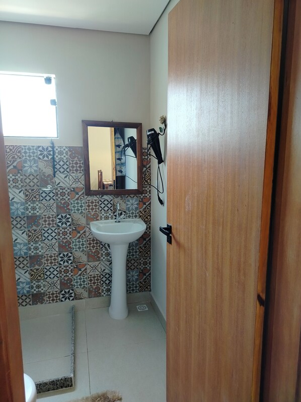 A bathroom with a tiled floor, a pedestal sink, a mirror, and a hairdryer on the wall. - Pouso Serra Santíssima (Tiradentes)