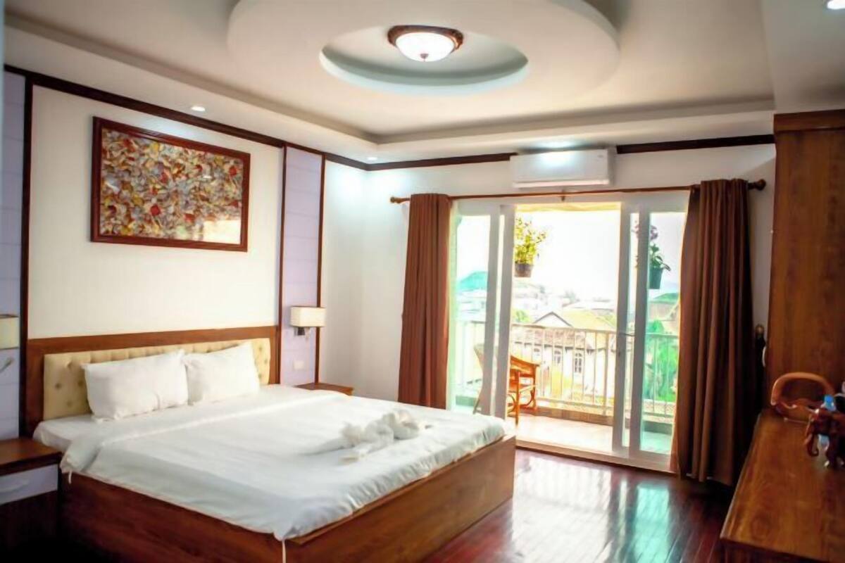 Una camera d'albergo con un letto, un quadro appeso al muro, una lampada a soffitto e una vista attraverso una porta scorrevole.