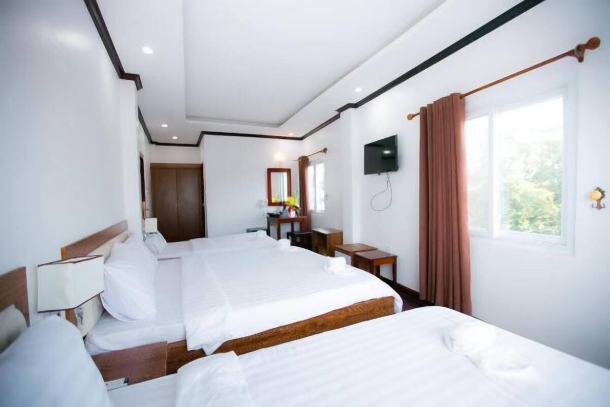 Una camera d'albergo con due letti, una TV, una scrivania e una finestra con tende.