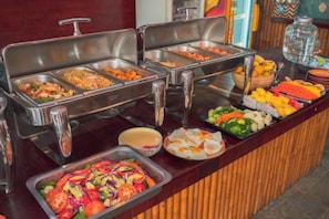 Un bufé con distintos alimentos y un recipiente de vidrio.