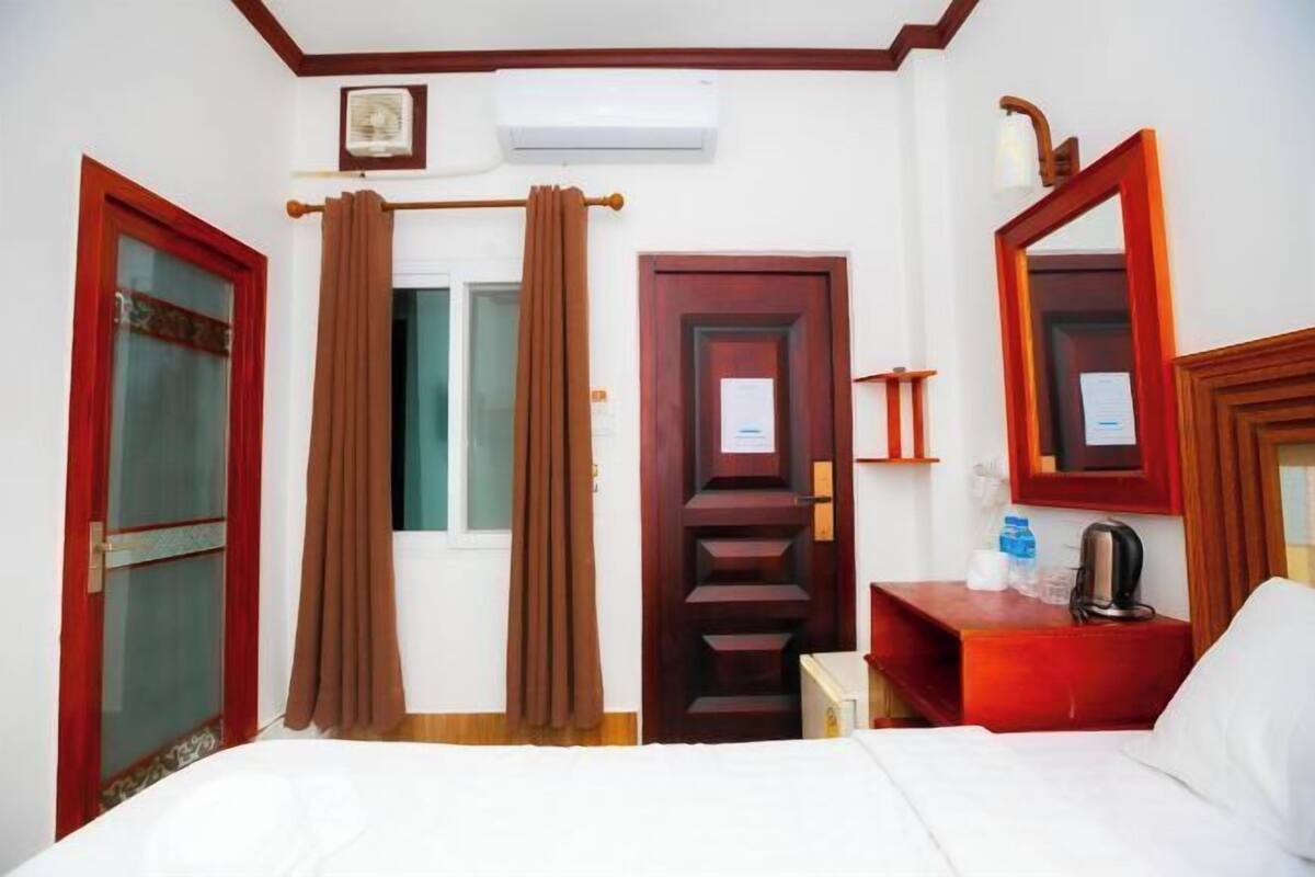 Una camera d'albergo con un letto, una scrivania con un bollitore, uno specchio e una porta con cornice rossa.