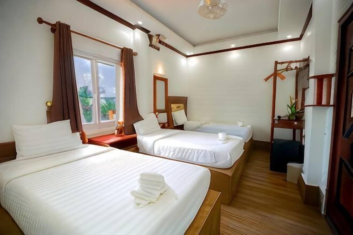 Una camera d'albergo con due letti, una finestra con tende, un comodino, uno specchio e una piccola pianta.