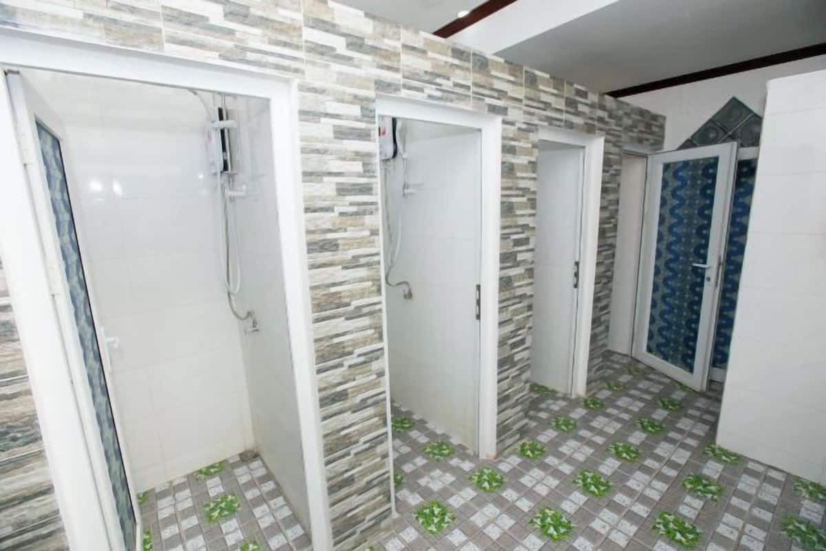 Un bagno con tre cabine doccia, ognuna dotata di una porta in vetro, e un pavimento piastrellato con un motivo a foglia verde.