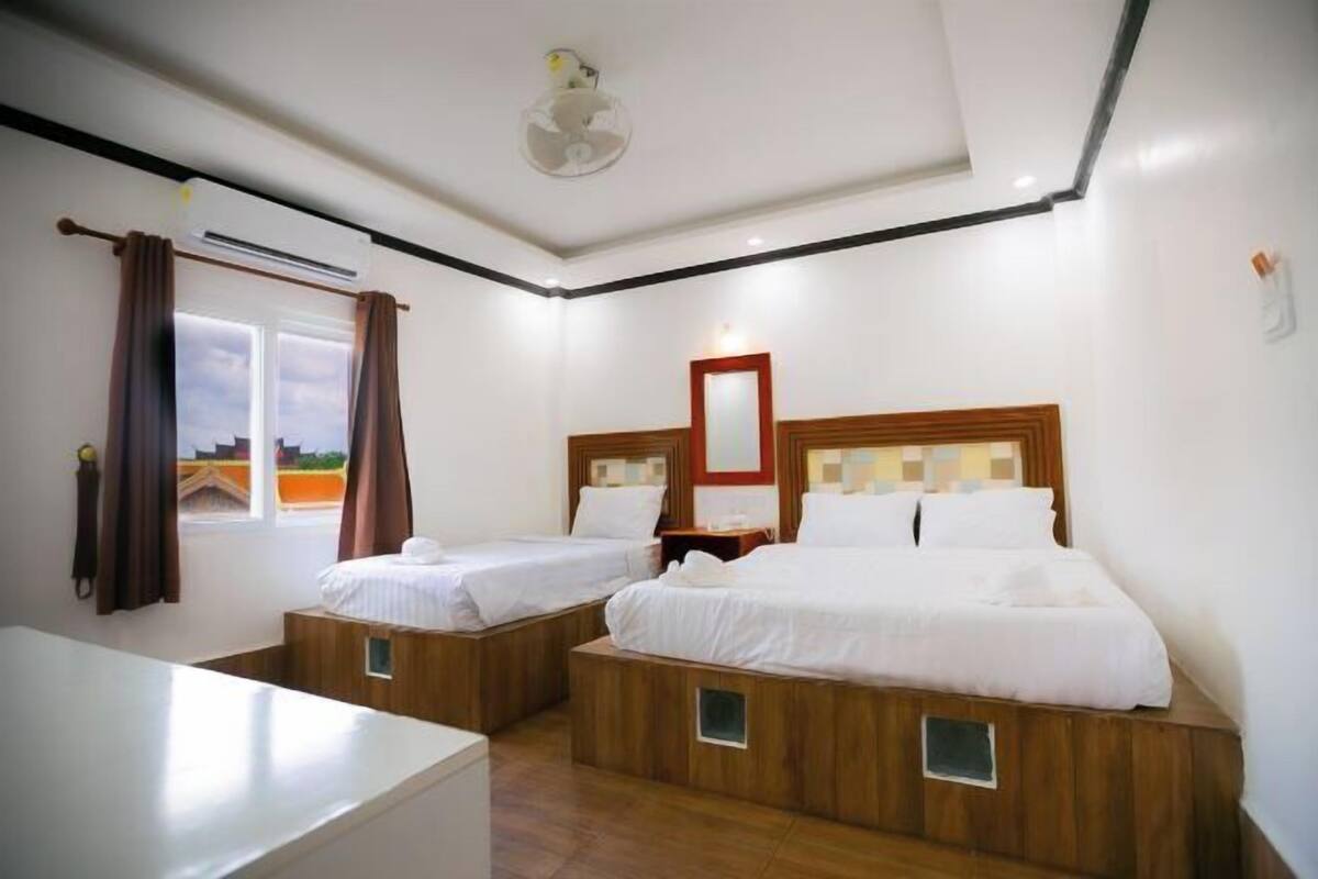 Una camera d'albergo con due letti, un climatizzatore, una ventola a soffitto e una finestra con tende.