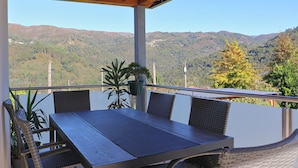 Ein überdachter Essbereich im Freien mit Tisch und Stühlen, mit Blick auf eine Berglandschaft.