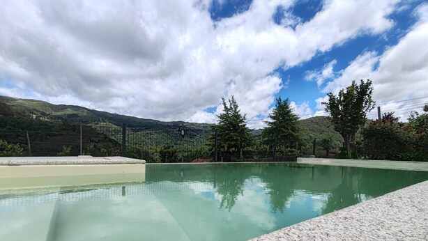 Ein Schwimmbecken mit freiem Blick auf die umliegende Landschaft, Bäume und ferne Hügel.