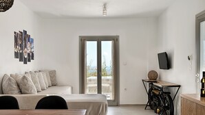 A modern bedroom with a bed, a desk with a bicycle, a TV, and a balcony with a view. - Aloft Suites Mykonos Island (Mykonos)
